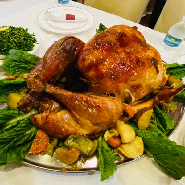 A whole roasted chicken, garnished with lettuce and vegetables, on a silver platter.