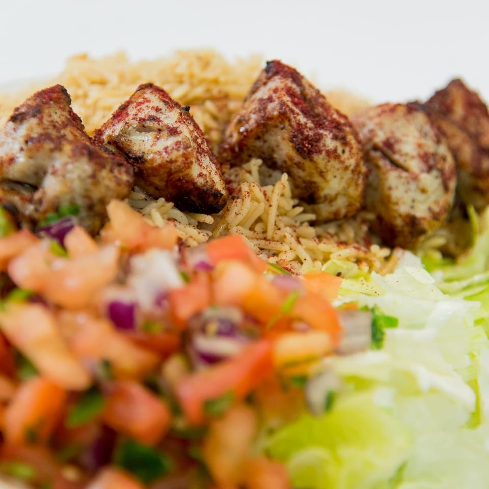Close-up of Ruz Bukhari's chicken kebab with rice, fresh tomato salsa, and lettuce.