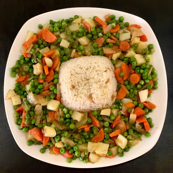 A white plate of Ruz Bukhari's rice surrounded by peas, carrots, and potatoes.