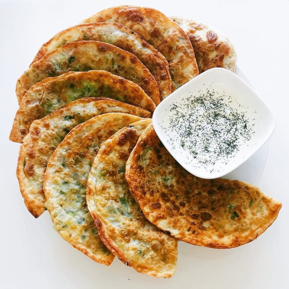 Golden-brown Afghan dumplings (Aushak) with green filling, arranged around a white bowl of yogurt sauce.
