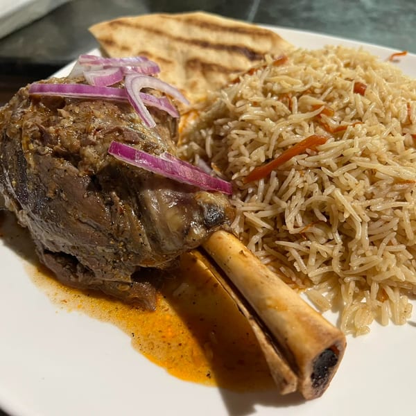 A Ruz Bukhari lamb shank with red onions, rice, and flatbread on a white plate.